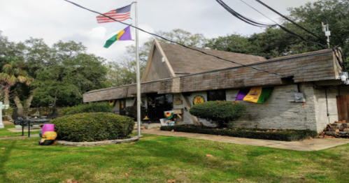 A building with a sloped roof, featuring an American flag and colorful banners, surrounded by greenery and a lawn.