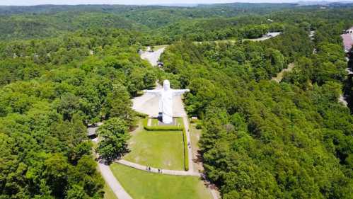 Aerial view of a large white statue of Christ surrounded by lush green trees and pathways.