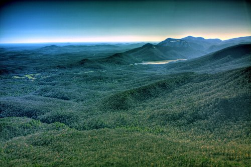 A panoramic view of lush green mountains and valleys under a clear blue sky, with distant peaks on the horizon.