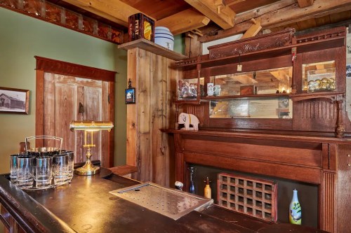 A rustic wooden bar with a vintage mirror, glassware, and decorative elements in a cozy interior setting.