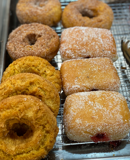 A variety of freshly baked donuts, including cinnamon sugar and jelly-filled, arranged on a cooling rack.