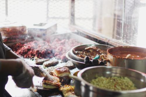 A chef prepares food in a busy kitchen, with various dishes and ingredients steaming on the grill and in bowls.