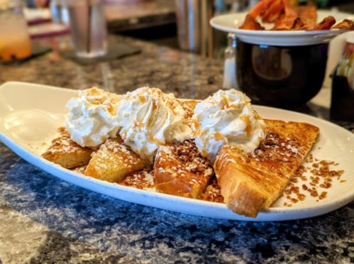 A plate of French toast topped with whipped cream and nuts, served with a side of syrup.