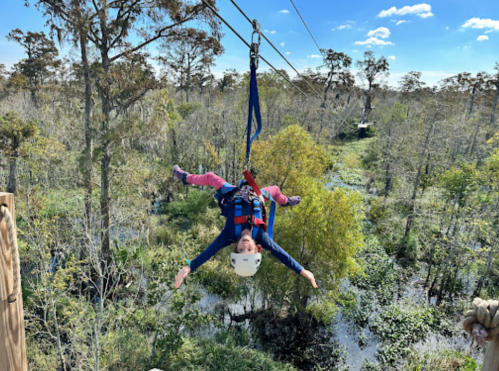 A child zip-lining through a lush, green landscape with trees and water below, enjoying an adventurous experience.