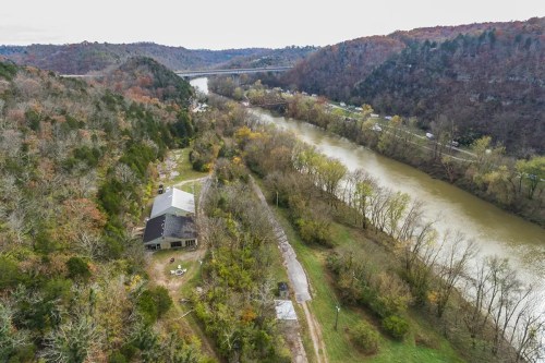 Aerial view of a river winding through hills, with a house and trees along the bank, showcasing autumn foliage.