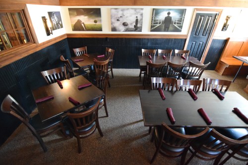A cozy restaurant interior featuring wooden tables and chairs, with dark walls and framed artwork.