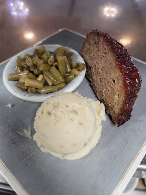 A plate with meatloaf, a serving of green beans, and a scoop of mashed potatoes.