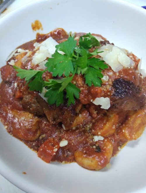A bowl of pasta with meat, topped with tomato sauce, grated cheese, and fresh parsley.