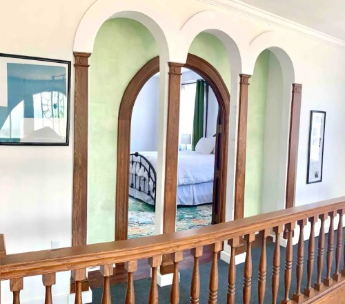 A hallway with arched doorways and wooden railings, leading to a room with a bed and green walls.