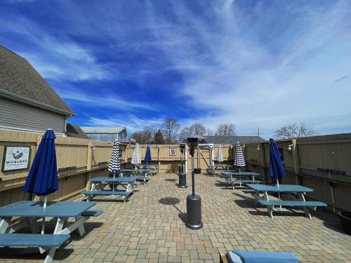 Outdoor patio with picnic tables, blue umbrellas, and a clear sky, surrounded by wooden fencing.