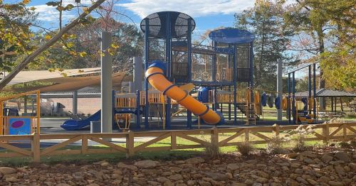 A colorful playground with slides and climbing structures, surrounded by trees and a grassy area.