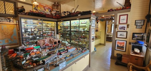 A model train exhibit featuring glass display cases, toy trains, and vintage posters in a cozy room.