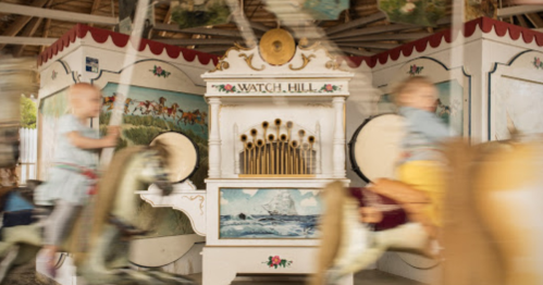 A vintage carousel with painted horses and a decorative organ, featuring children riding and blurred motion.