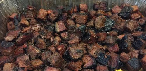 Close-up of diced, charred beef brisket pieces in a metal tray, showcasing a smoky, grilled texture.