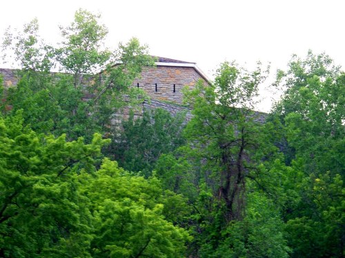 A stone building partially obscured by lush green trees under a bright sky.