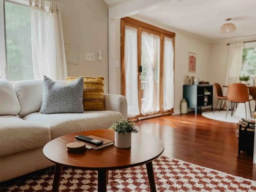 Cozy living room with a white sofa, wooden coffee table, and a dining area featuring brown chairs and large windows.
