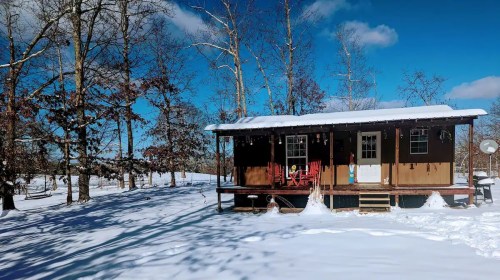 A cozy cabin surrounded by snow, with a clear blue sky and trees in the background.
