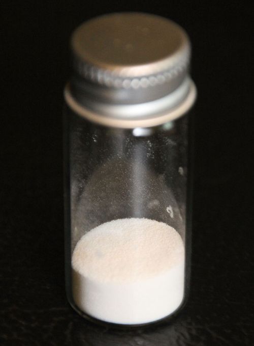 A clear glass vial with a silver cap, containing a small amount of white powder at the bottom.