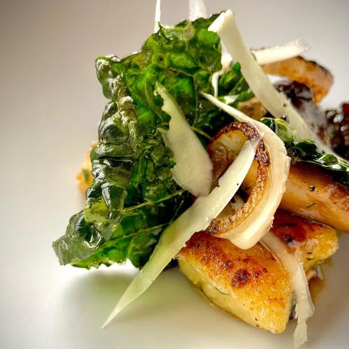 A close-up of a gourmet dish featuring sautéed greens, crispy onions, and tender protein on a white plate.
