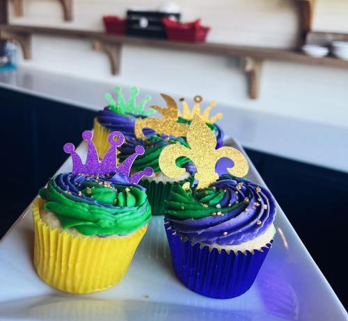 Colorful cupcakes with purple and green frosting, topped with crown and fleur-de-lis decorations, on a white plate.