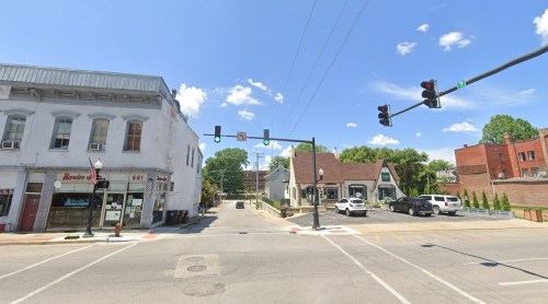 A street view showing a traffic light, buildings, and parked cars under a clear blue sky.