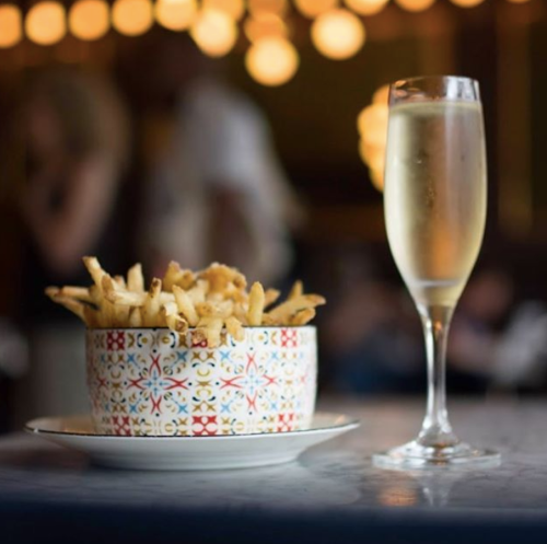 A bowl of golden fries next to a glass of sparkling wine, set against a softly lit background.