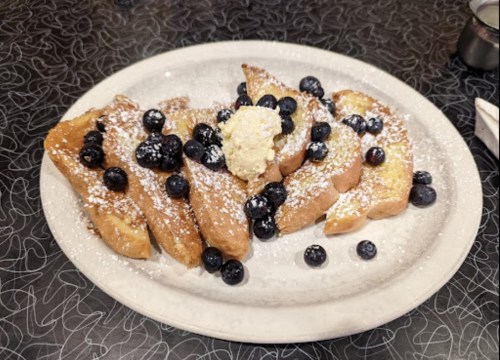 A plate of French toast topped with blueberries and a dollop of butter, dusted with powdered sugar.