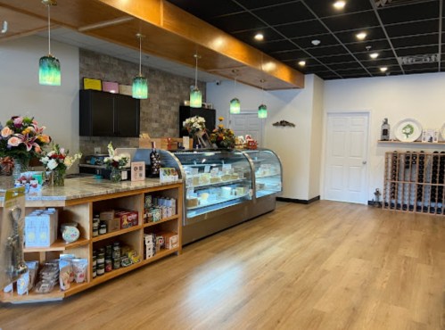 Bright, modern shop interior with a display case, wooden shelves, and decorative lighting. Flowers add a welcoming touch.