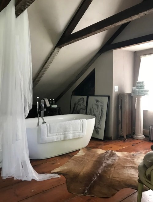 A cozy bathroom with a freestanding tub, wooden beams, and art on the wall, featuring a warm, rustic atmosphere.