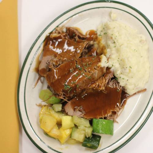 A plate of sliced roast beef with gravy, mashed potatoes, and mixed vegetables including zucchini and pineapple.