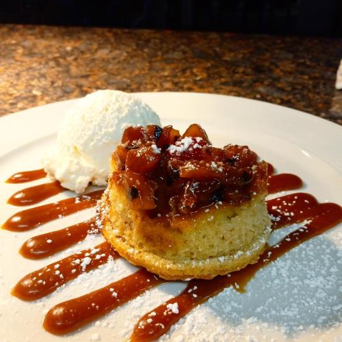 A slice of cake topped with caramelized fruit, served with a scoop of ice cream and drizzled with sauce.