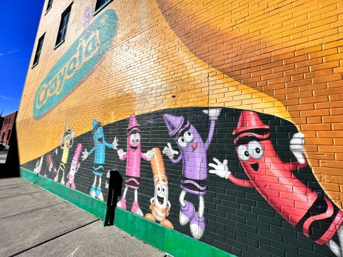 Colorful mural of animated crayons on a brick wall, featuring various characters in vibrant colors and playful poses.