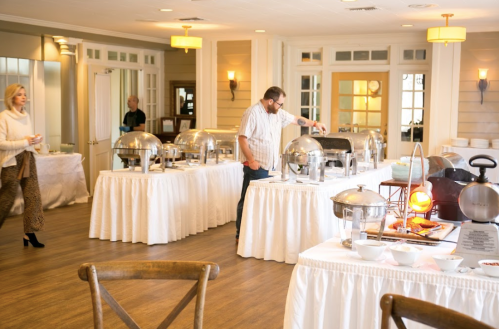 A dining area with buffet tables, a man serving food, and a woman holding a drink in the background.