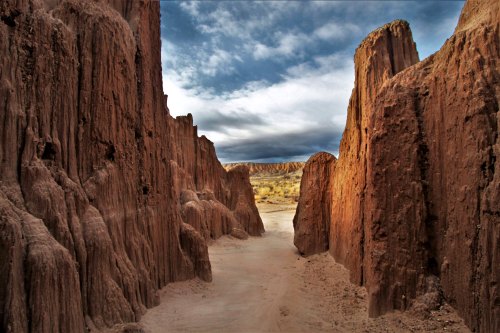 A narrow canyon with towering, rugged rock formations under a cloudy sky.