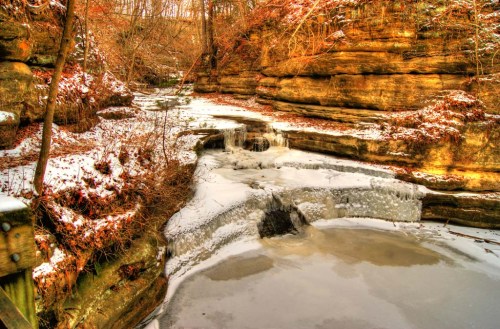 A serene winter scene of a frozen creek surrounded by snow-covered rocks and trees.