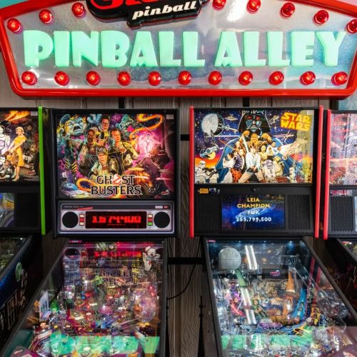 Colorful pinball machines featuring "Ghostbusters" and "Star Wars" in a vibrant arcade setting.