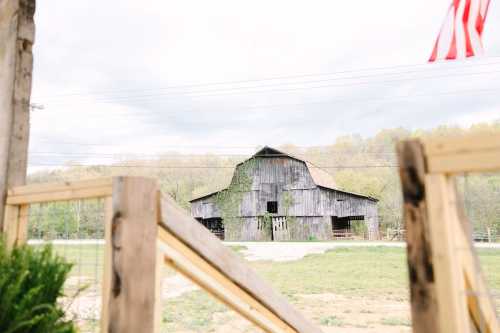 A weathered barn covered in greenery, set against a cloudy sky and surrounded by open fields. An American flag is visible.