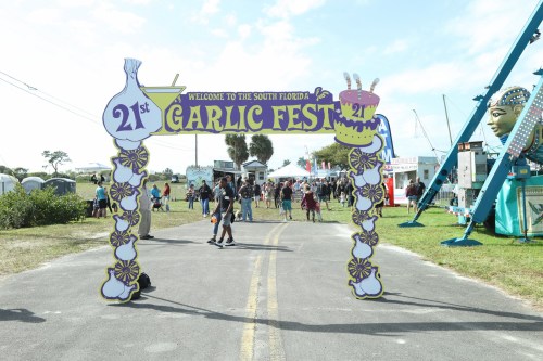 A colorful archway welcomes visitors to the 21st South Florida Garlic Fest, with festival activities in the background.