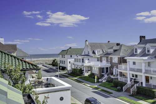 A coastal neighborhood with charming houses, green lawns, and a view of the ocean under a clear blue sky.