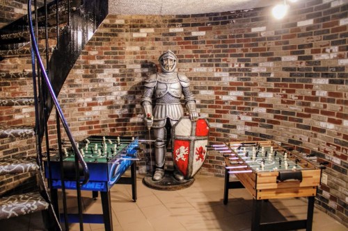 A basement game room featuring a knight statue, a foosball table, and a chess table against a brick wall.