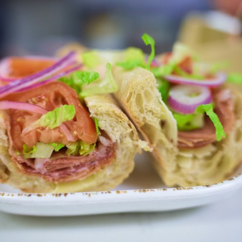 A close-up of a sandwich filled with lettuce, tomato, onions, and layers of deli meats on a soft roll.