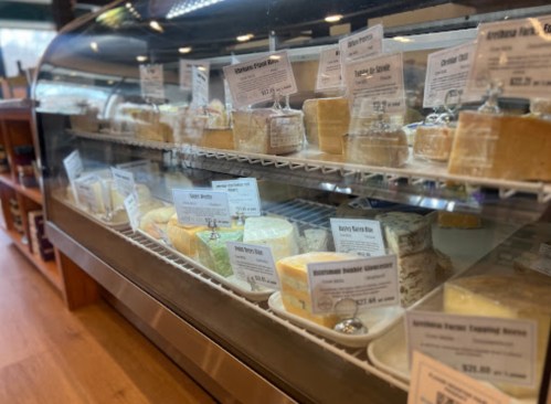 A display case filled with various cheeses, each labeled with names and prices.
