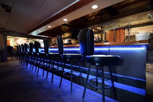 A dimly lit bar with black stools and blue LED lighting along the counter, creating a cozy atmosphere.