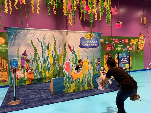 A colorful ocean-themed backdrop with children posing for a photo, surrounded by seaweed and playful sea creatures.