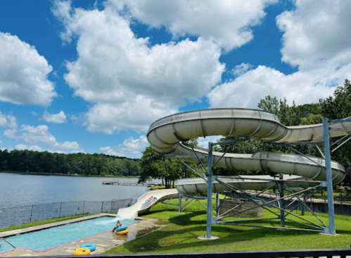 Water slides beside a pool and lake, with blue skies and fluffy clouds in the background.