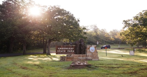 Sign for Greenleaf State Park surrounded by trees and morning sunlight, with a misty landscape in the background.