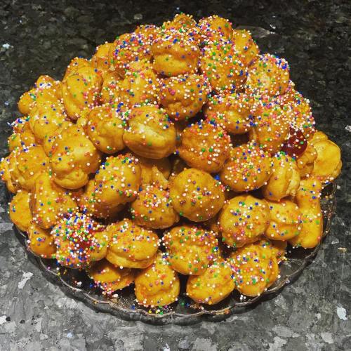 A large pile of golden, round pastries topped with colorful sprinkles on a glass plate.