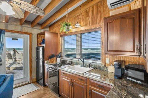 Cozy kitchen with wooden cabinets, granite countertops, and a view of the beach through large windows.