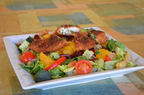 A colorful salad topped with crispy chicken, cherry tomatoes, cucumbers, and various vegetables on a white plate.