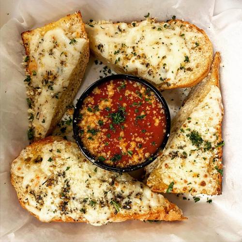 Toasted garlic bread slices topped with cheese, served with a small bowl of marinara sauce, garnished with herbs.